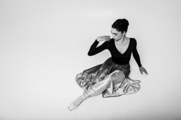 young pretty, beautiful ballerina in a long blue dress sitting on the floor tired on a light background. Art, inspiration concept. Classical ballerina in pointe shoes and dress. Black and white photo.