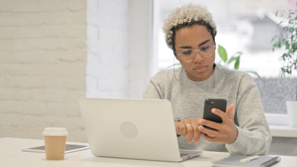 African Woman using Smartphone while using Laptop in Office
