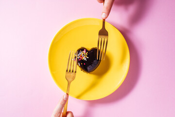 Heart shaped chocolate cake on a yellow plate with heart shaped chocolate pralines on a purple background with two red ribbons. Great concept for Valentine day or anniversary of love or wedding