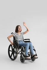 Plakat Young woman in wheelchair waving hand on light background