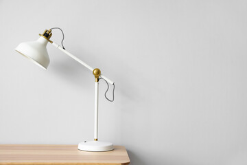 Modern white lamp on wooden table near light wall