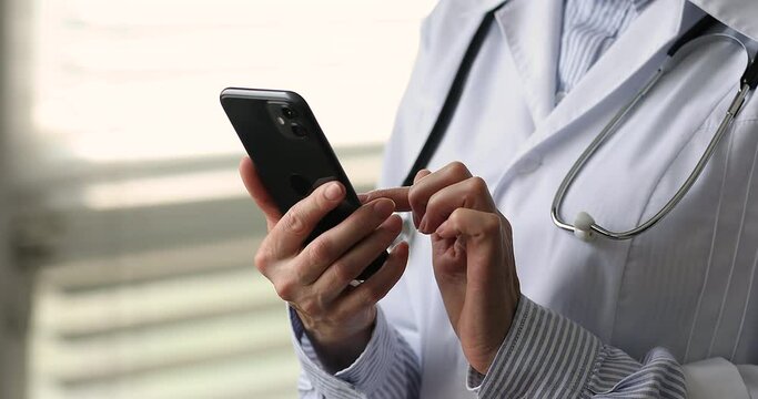 Close up female therapist in coat standing in clinic office holds in hands cellphone, use mobile app, check medical appointments, virtual assistance software, modern wireless tech, healthcare concept