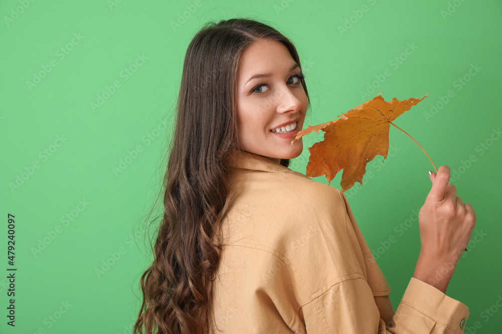 Wall mural Portrait of woman holding beautiful autumn leaf on green background