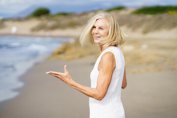 Fototapeta na wymiar Smiling mature woman walking on the beach, spending her leisure time, enjoying her free time