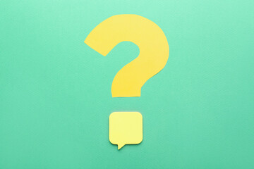 Question mark made of yellow paper with sticky note on green background