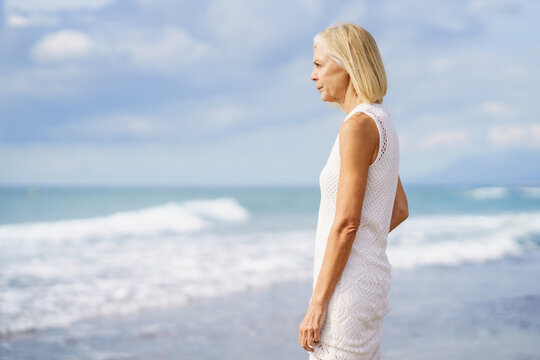 Mature Woman Gazing Serenely At The Sea. Elderly Female Standing At A Seaside Location