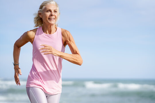 Older female doing sport to keep fit. Mature woman running along the shore of the beach.