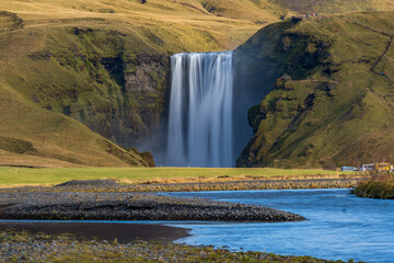 Long exposure of famous Skogafoss waterfall in Iceland from the distance with hikers and blurred cars
