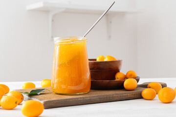 Jar of tasty kumquat jam and fresh fruits on kitchen table