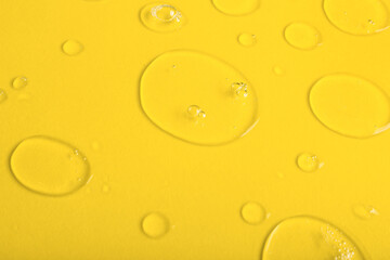 Drops of liquid transparent gel with bubbles on yellow background, closeup