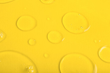 Drops of liquid transparent gel with bubbles on yellow background, closeup