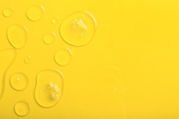 Many drops of liquid transparent gel with bubbles on yellow background