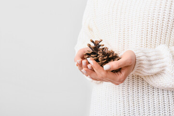 Woman holding beautiful pine cones on light background, closeup