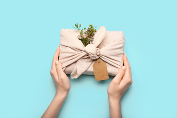 Female hands with gift box wrapped in fabric on color background, closeup