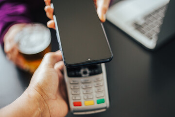 Woman paying a bill through a smartphone using NFC technology in a restaurant. Satisfied customer paying via mobile phone using contactless technology. Close up mobile payment hands in a coffee shop