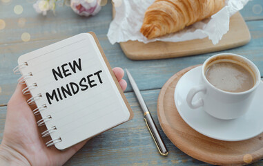 New Mindset text on notepad in woman hand with Croissants and Coffee