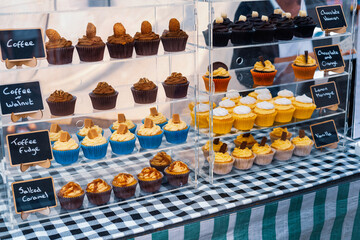 Coffee and walnut cupcakes on sale with other cupcake flavours on glass shelves at an outdoor store - 479243648