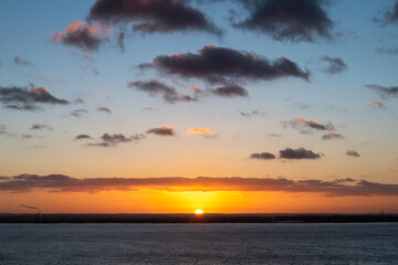 Beautiful sunset over Sandwich as seen from Ramsgate, Kent, UK. The Sun is just disappearing behind the horizon. There are some puffy clouds catching the gold of the sun.