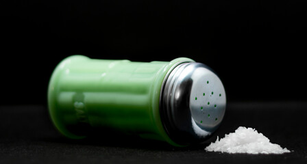 Salt shaker with some salt next to it