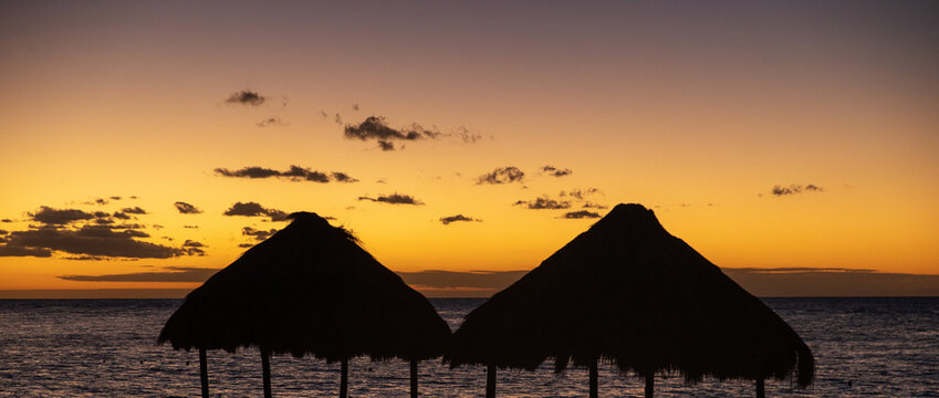 Silhouette of palm thatch roof hut next to Caribbean sea during colorful sunset on the tropical island of Cozumel, Mexico. 
