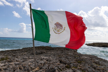 National flag of Mexico blows in the wind on a limestone beach on the tropical island of Cozumel.