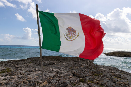 National flag of Mexico blows in the wind on a limestone beach on the tropical island of Cozumel.