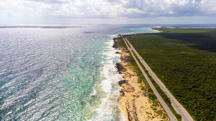 Aerial drone view of coastal highway adjacent to dense jungle and Caribbean sea on the tropical island of Cozumel, Mexico. The ocean waves are crashing against the sandy beach.