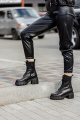 A slender woman in black leather boots, black trousers. Collection of shoes for women