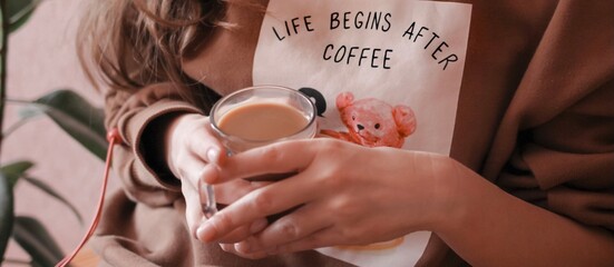 A cute beautiful young woman with a cup of coffee. Life begins after coffee is written on the sweatshirt. Drinking coffee with milk. Banner/	