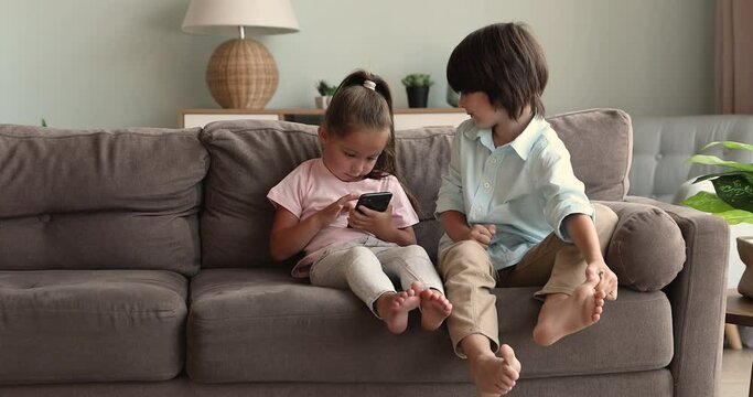 Funny small children diverse siblings boy girl stay at home alone enjoy using modern tech cell play web game in app browse internet. Friendly elder brother younger sister kids make phonecall on gadget