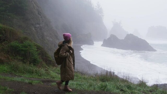 People on adventure, freedom and happiness concept, slow motion shot RED camera. Happy hiker woman enjoying calm rainy day on rocky Oregon coast. Looking around while exploring scenic nature landscape