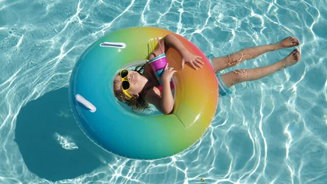 Happy kid playing with colorful swim ring in swimming pool on summer day. Child water toys. Children play in tropical resort. Family beach vacation.