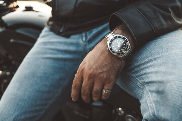 Male wrists, expensive watch close-up. Hands of young man sitting on motorcycle. Concept of luxury...