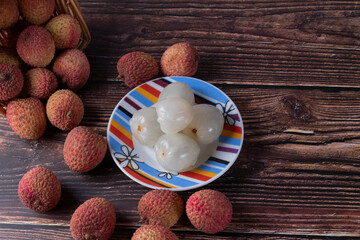 Tasty Lychee (Litchi chinensis, scientific name in Latin) on a wooden table with some without their shells served on a colorful saucer. Selective focus.