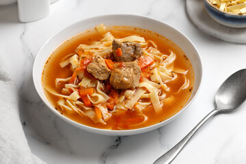 Lagman. The national Uzbek soup with noodles and pieces of meat, fried vegetables. Close up soup. White plate and white background