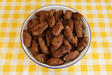 Fresh fried long meatballs of "Soutzoukakia smyrneika" Greek food on a plate on a white-yellow checker tablecloth. Top view, selective focus
