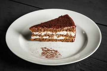 Piece of chocolate cake on a white plate. Black wooden background.