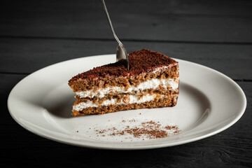 Piece of chocolate cake on a white plate. Black wooden background.