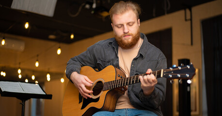Obraz premium A young guy with a beard plays an acoustic guitar in a room with warm lighting