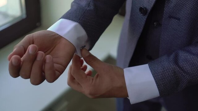 A man is fastening a button on a gray jacket. Male wears a classic suit. Businessman, office worker or groom. Person adjusting sleeves of his white shirt with cufflinks.