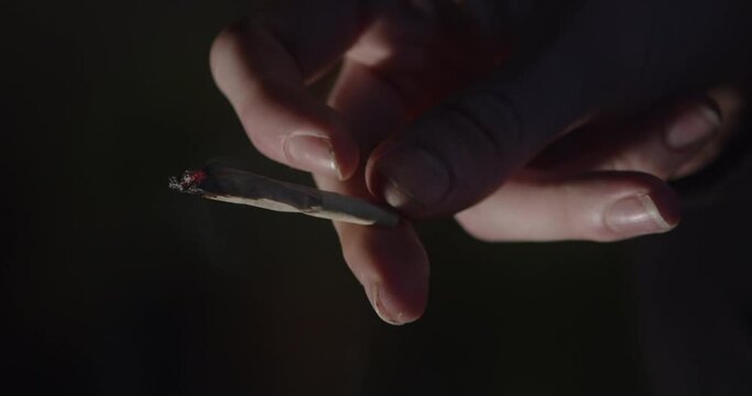 Male Hand Holding Smoking Burning Cannabis Joint in Darkness, Close up Shot
