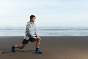Hispanic teenager stretching at the beach while is focused on his goals