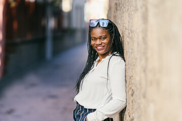 African woman with sunglasses on the head leaning against a wall outdoors