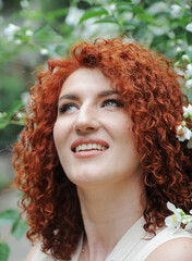 Young beautiful red-haired woman in blossoming flowers garden. 