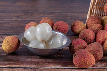 Tasty Lychee (Litchi chinensis, scientific name in Latin), on a wooden table with some without shells, served over stainless steel bowl. Selective focus.