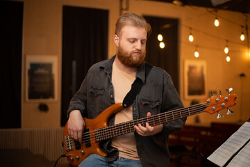 A young guy with a beard plays a bass guitar with five strings