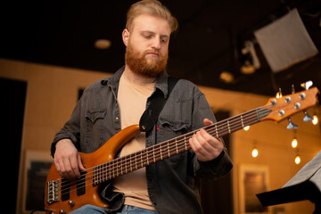 Obraz premium A young guy with a beard plays a bass guitar with five strings