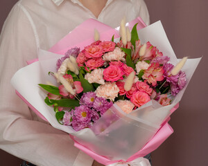 a girl in a white shirt holds a large bouquet of flowers of pink roses, pink carnations, purple chrysanthemum, lagurus