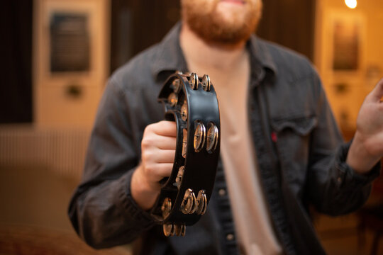 A young guy with a beard plays the tambourine