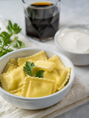 Serving of ravioli with butter and a sprig of fresh parsley, sour cream sauce and a drink on a white plate. Close-up. White background. Restaurant, cafe, hotel, home cooking.